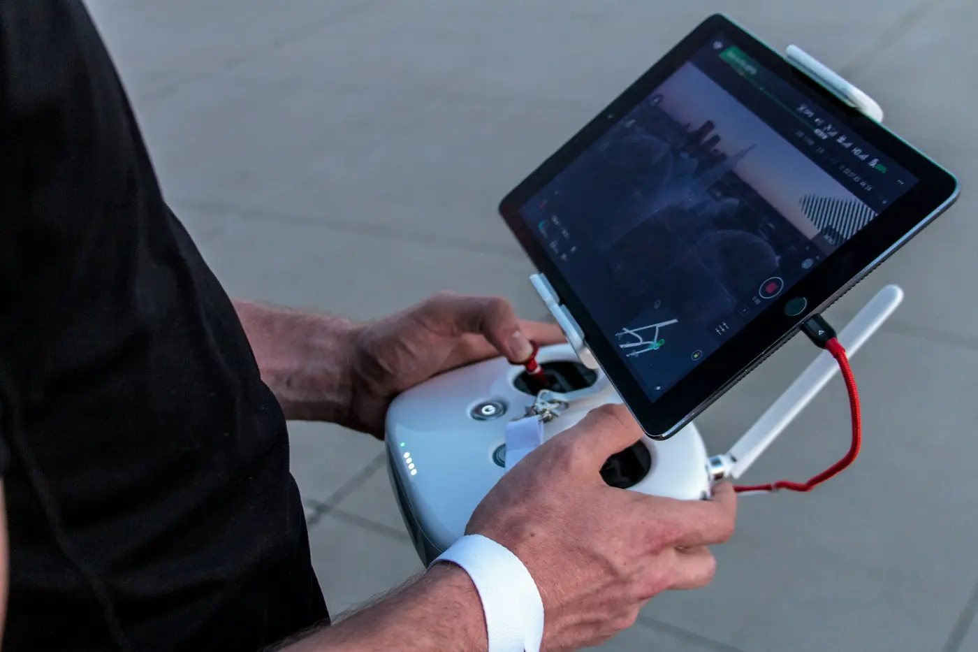Hands holding a drone controller with a tablet showing the camera view