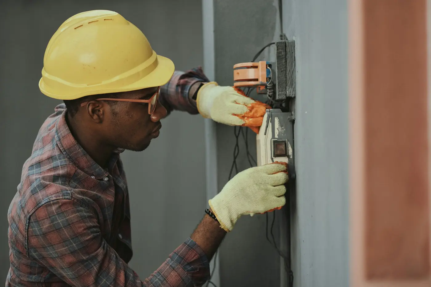 An electrician in a yellow hard hat and gloves working on wiring