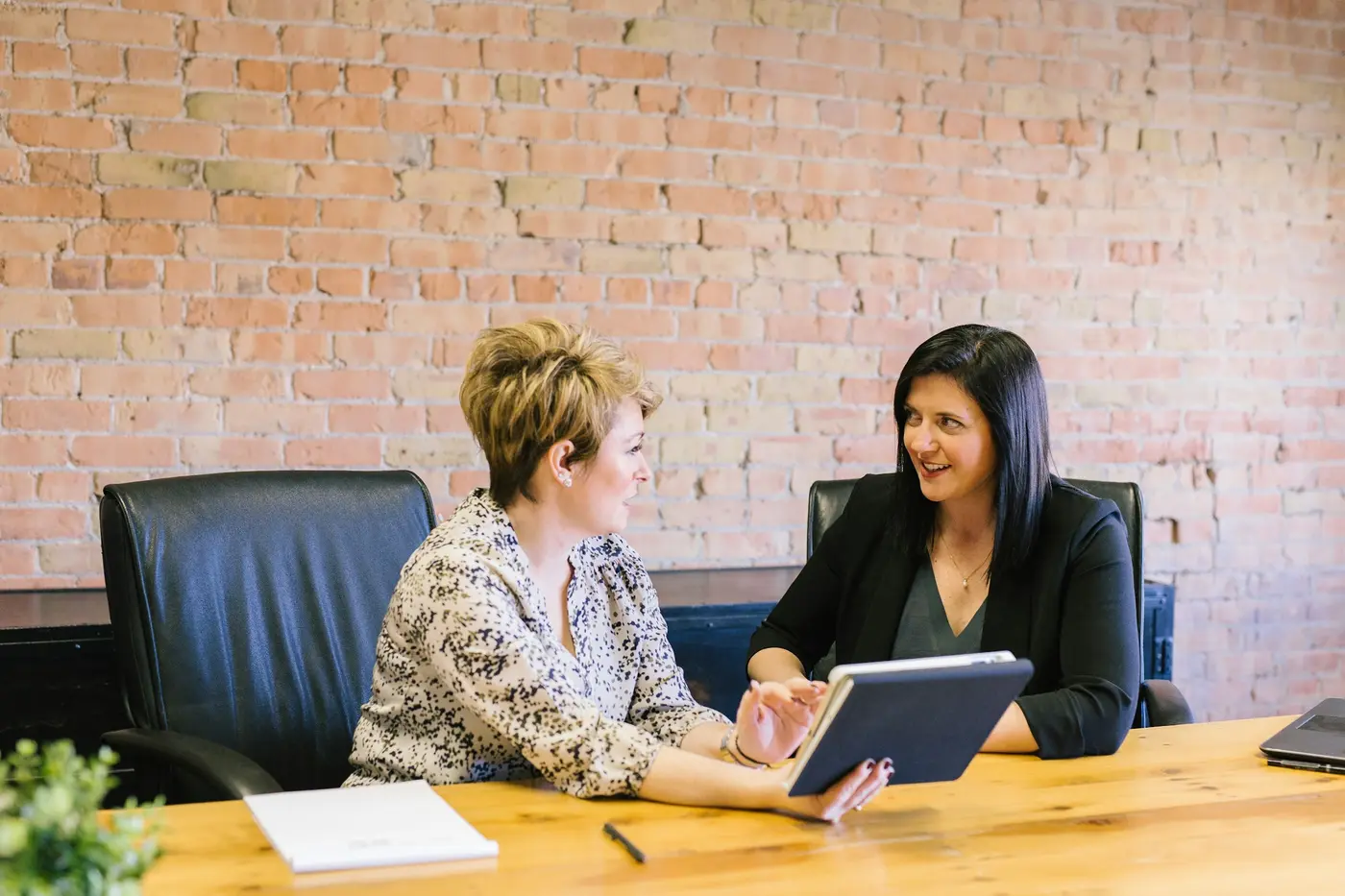 Two women talking over a tablet at a table in an office