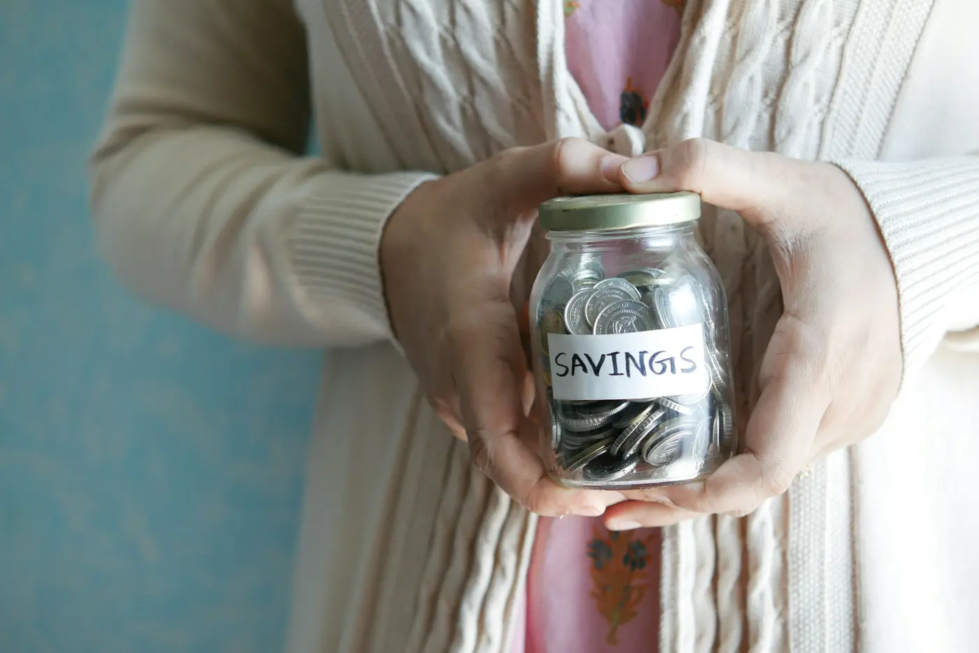 Hands holding a jar of coins labeled savings