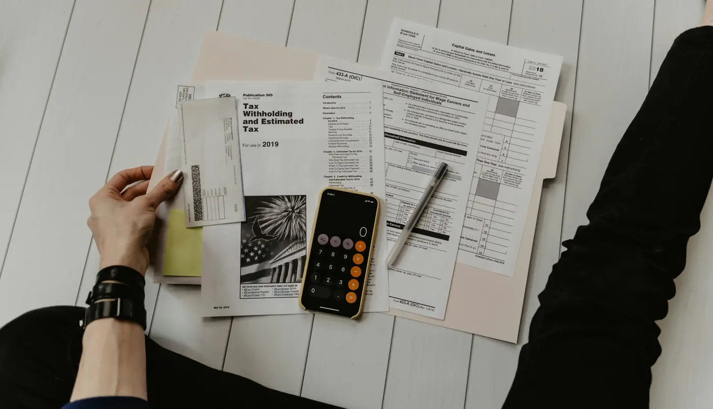 Hands going through tax forms with a phone calculator on a desk