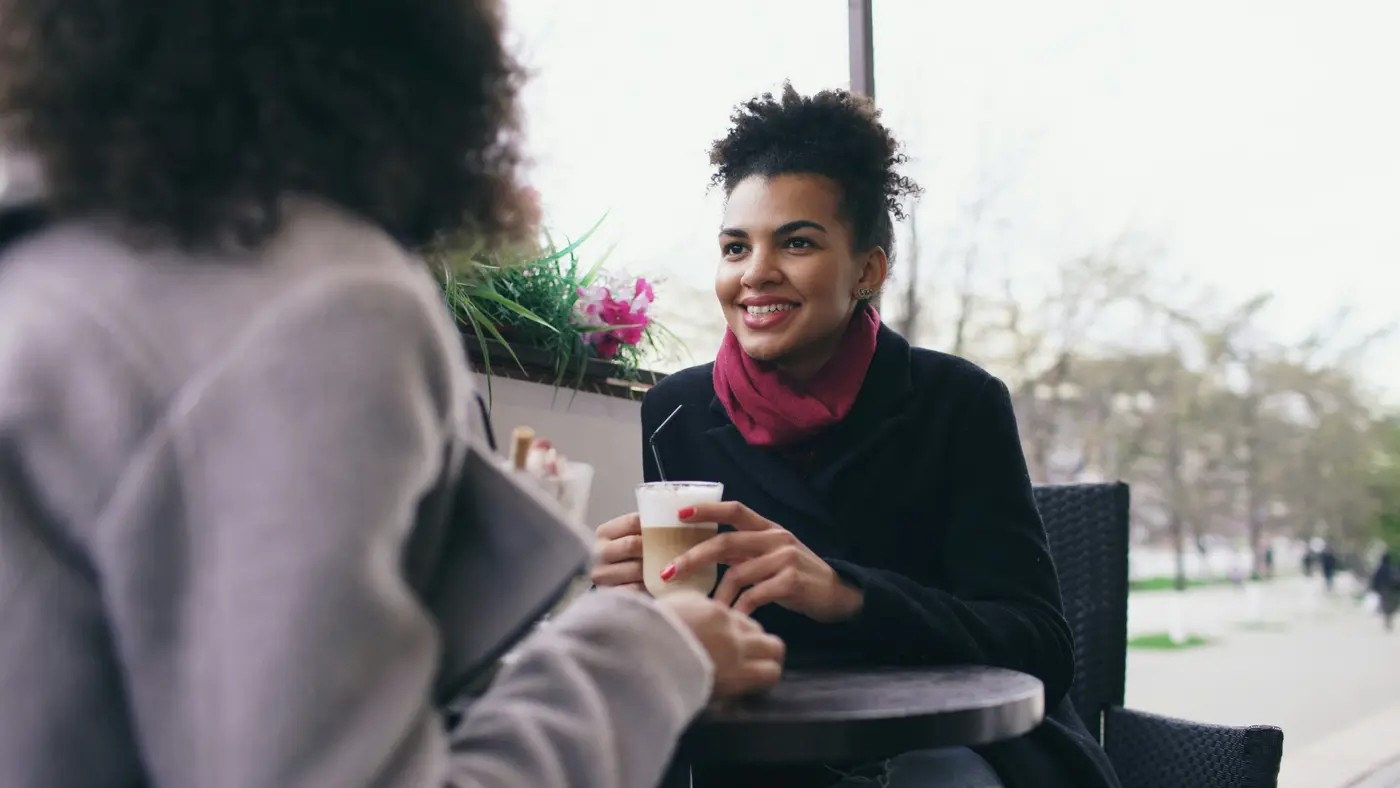 A smiling woman talking with a friend over coffee at a cafe